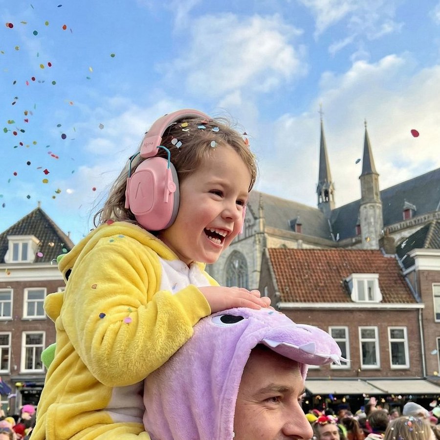 Girl in a yellow dinosaur onesie with pink Alpine earmuffs on her father's shoulders under falling confetti