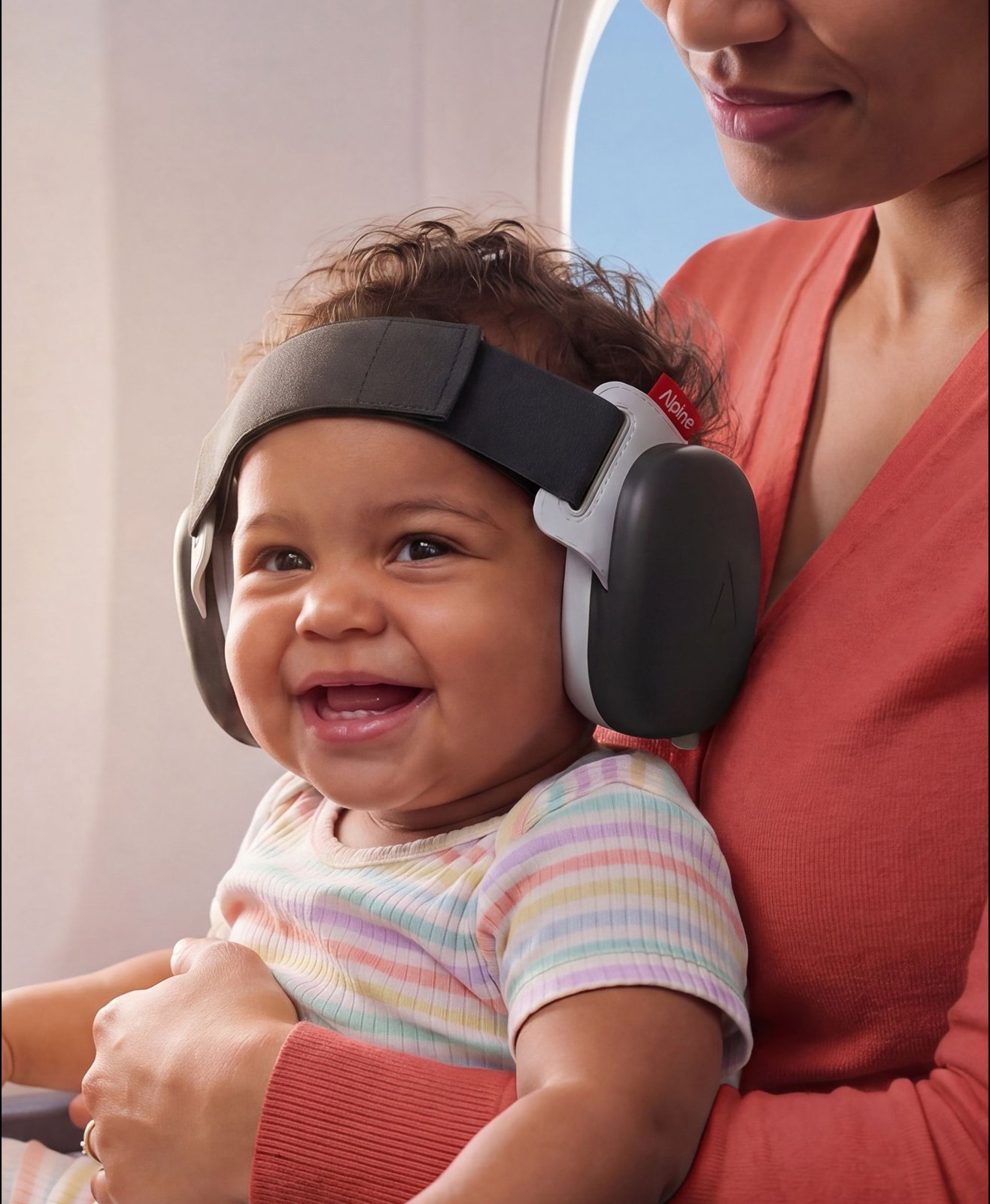 Laughing baby wearing black Muffy Baby earmuffs on their mother's lap